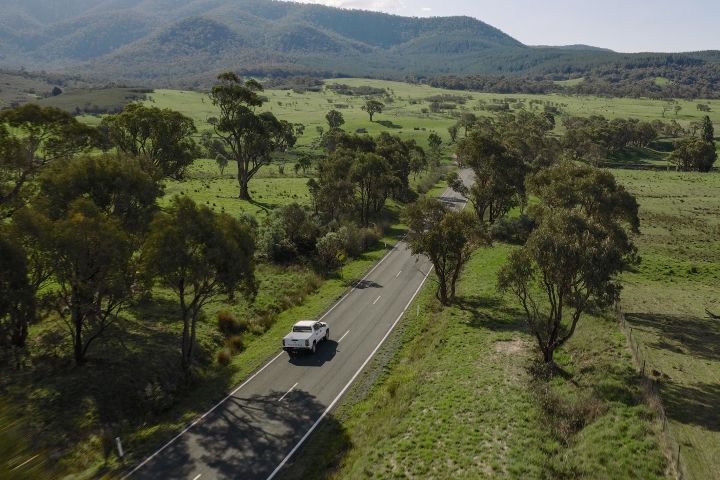 2026 Nissan Navara SL dual cab ute finished in Alpine White captured from an elevated rearward angle on an open road through a wide rural valley.