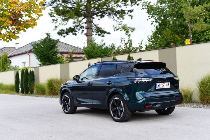 3/4 Heckansicht eines dunkelgrünen Nissan Qashqai e‑Power, der am Straßenrand vor einer hellen Mauer steht