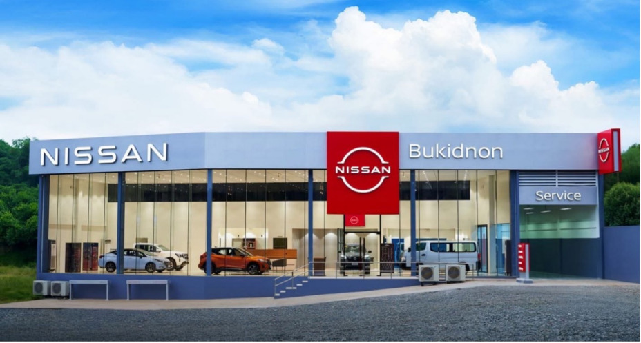 Exterior of the Nissan Bukidnon dealership with a modern glass facade, featuring a large red and white Nissan logo on the building.
