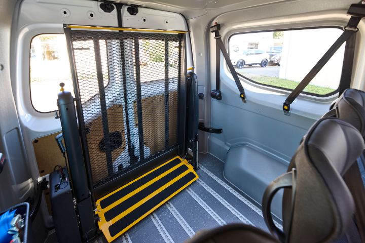 Blick über die dritte Sitzreihe im Inneren des Nissan Interstar-e mit MobiTEC Ausbau auf den eingeklappten Rollstuhllift im Fahrzeugheck.
