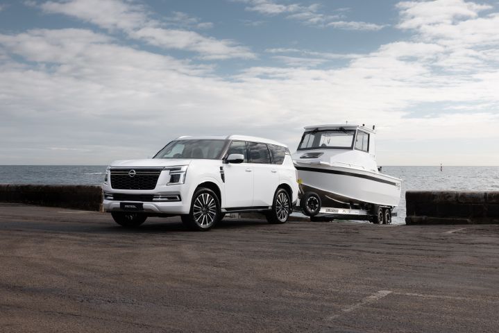 2026 Nissan Y63 Patrol finished in white, shown from a close front three-quarter exterior angle towing a large white boat on a trailer at a coastal boat ramp.