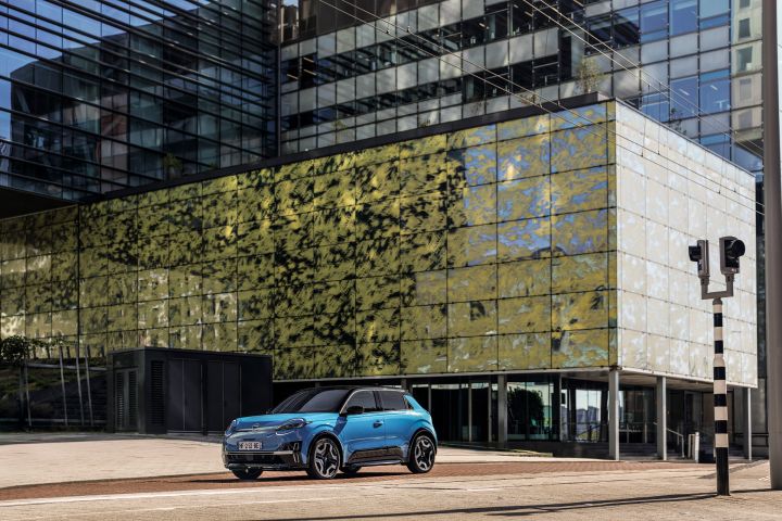 Ein blauer Nissan Micra parkt in Rotterdam vor einem Gebäude mit teilweise grün bemalter Glasfassade.