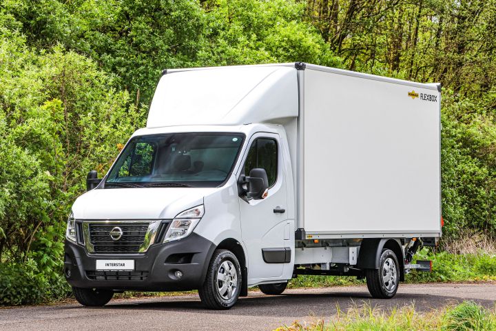 Ein weißer Nissan Interstar mit Kofferaufbau steht schräg vor grünen Bäumen