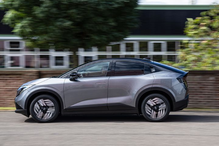 Seitliche Fahraufnahme eines grauen Nissan Leaf, im Hintergrund ist eine halbhohe Backsteinmauer und ein Industriegebäude zu sehen