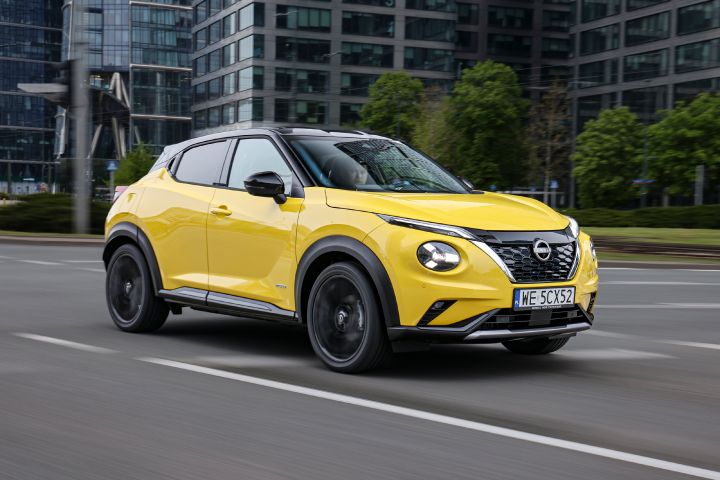 Jadący żółty Nissan Juke (widok z półprofilu) z budynkami w tle