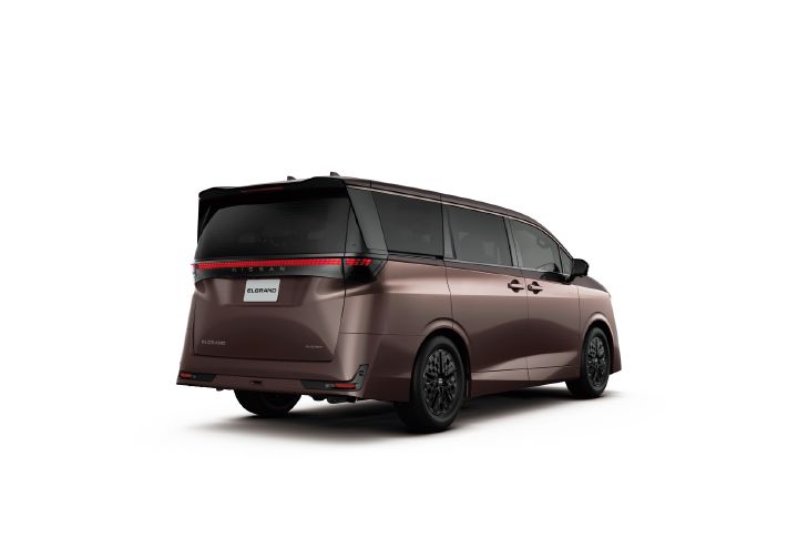 A studio image of the All new ELGRAND in a dark brown metallic finish with a subtle burgundy tone, set against a light gray background. The vehicle is shown facing right from a rear-left three-quarter angle, revealing the left side profile and rear design. A black roof and dark-tinted windows create a distinctive two-tone appearance. The rear features a full-width red LED light bar with the “NISSAN” lettering integrated across the tailgate. Sculpted body surfaces, a sharp rear-end design, and black alloy wheels emphasize the premium character and strong visual presence of the minivan.