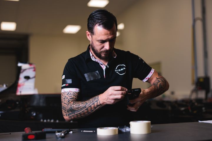 Ein Mechaniker im schwarzen Nissan Shirt macht ein Foto von einem Bauteil auf einem Tisch