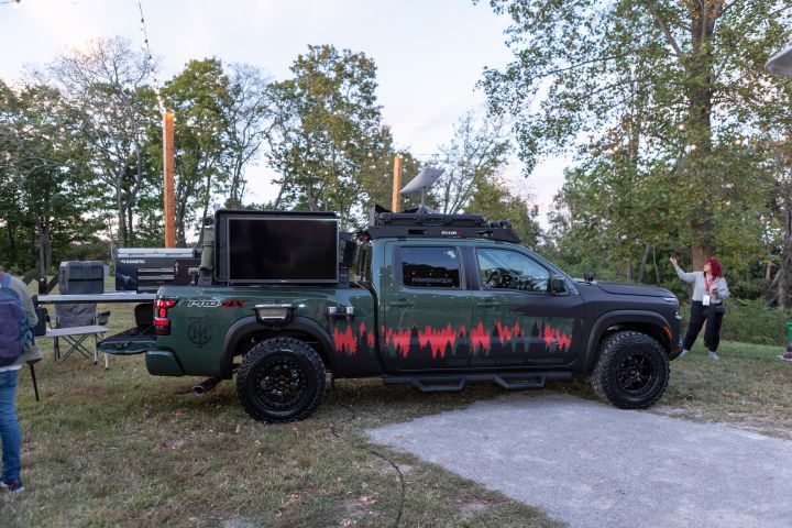 A profile view of a 2025 Nissan Frontier Trailgater edition parked on grass with people and trees behind.