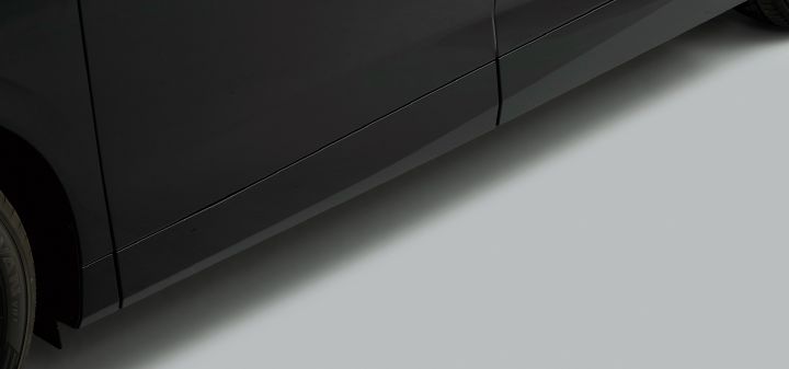 ブラックのエルグランド ステップタイプの助手席側下部を、車両側面からクローズアップで撮影した画像。画面左側にはブラックのボディパネルとリアタイヤの一部が見え、車両は右方向へ伸びる向きで配置されている。スライドドアは閉じられた状態で、電動ロングステップは格納されており、サイドシル下部にすっきりと収まっている。
ボディ表面は光沢のあるブラックで、照明を受けて滑らかな反射や陰影が生まれている。ドアの継ぎ目や下部のキャラクターラインが確認でき、シンプルで一体感のある側面デザインが強調されている。