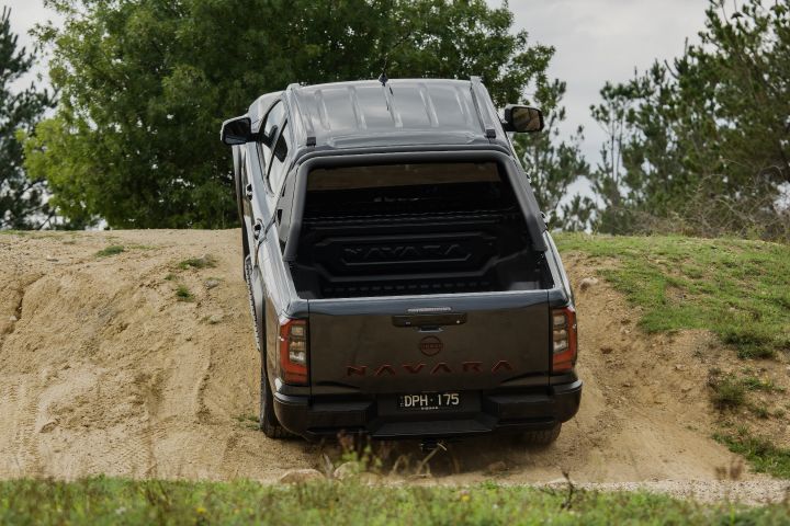 2026 Nissan Navara PRO-4X finished in Boulder Grey captured during a steep rear ascent with NAVARA tailgate lettering, tall tail‑lamps and grassy crest ahead.