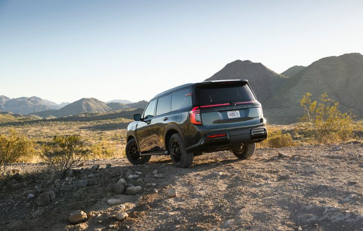Rear angled view of a 2025 Nissan Armada PRO-4X parked on rocky terrain, other rocky hills and mountains are behind.