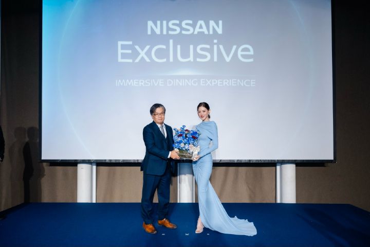 Nissan executive and Baifern standing on stage at the Nissan Exclusive Immersive Dining Experience event, holding a blue-themed floral arrangement in front of a large event backdrop