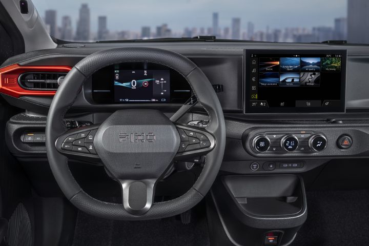 Photograph showing PIXO cockpit with leather steering wheel, digital instrument cluster, and wide infotainment touchscreen. Red-trimmed vents, physical climate controls, hazard button, and steering-wheel controls highlight sporty design and connected driving features.