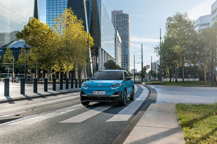 Ein blauer Nissan Micra fährt vor Hochhäusern durch das Zentrum von Rotterdam
