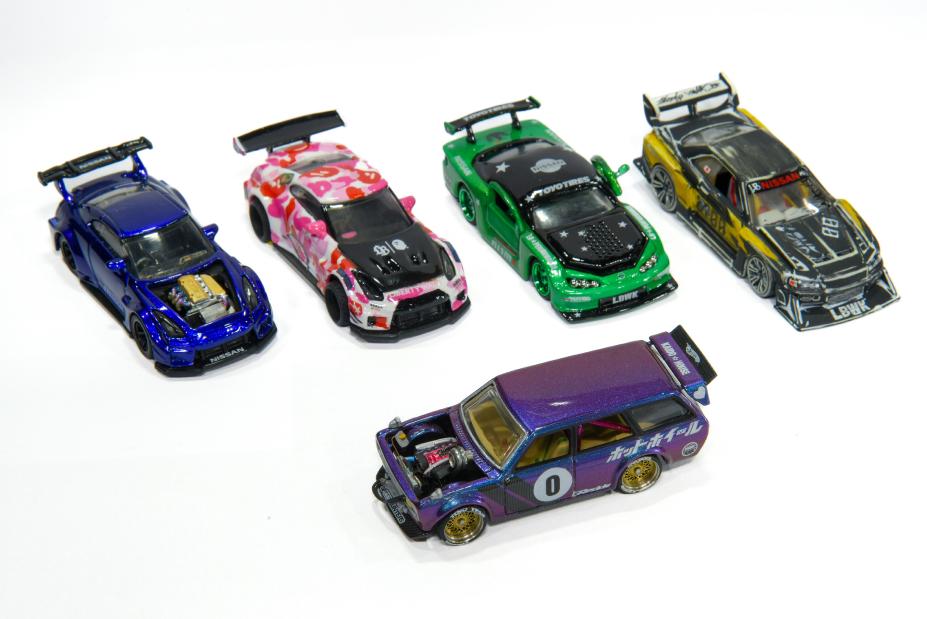 Cinco miniaturas de carros coloridos e detalhados sobre uma superfície branca, cada uma com design e adesivos únicos