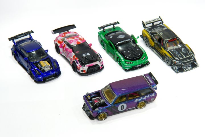 Cinco miniaturas de carros coloridos e detalhados sobre uma superfície branca, cada uma com design e adesivos únicos