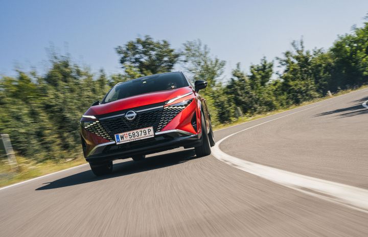 Blick von schräg unten auf einen Nissan Qashqai in Fuji Sunset Red, der dynamisch durch eine Landstraßenkurve fährt