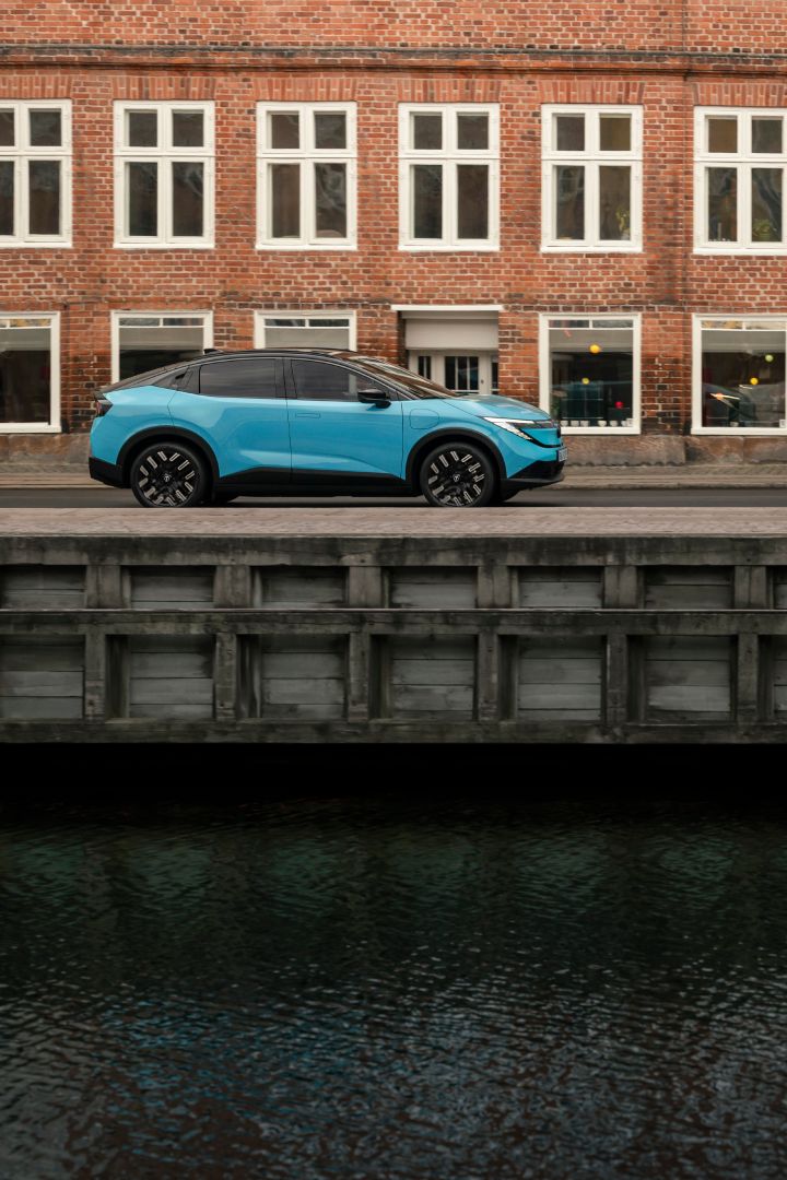 An einem Kanal in Kopenhagen steht seitlich ein türkiser Nissan LEAF, dahinter ein rotes Backsteingebäude