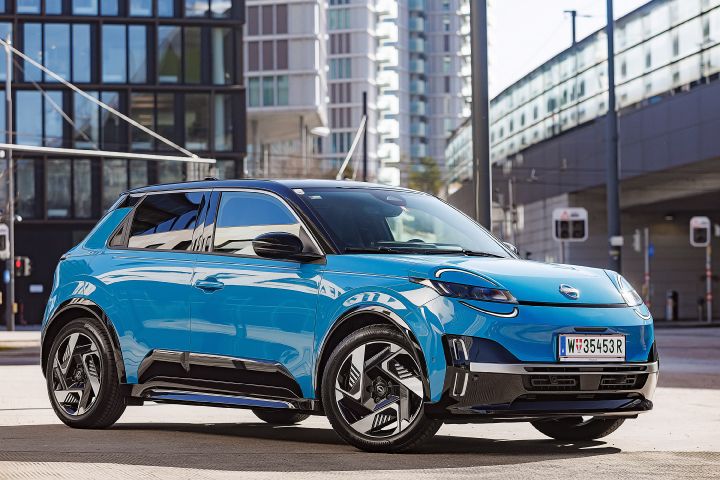 3/4 Frontansicht eines leuchtend blauen Nissan Micra mit schwarzem Kontrastdach vor städtischen Hochhäusern