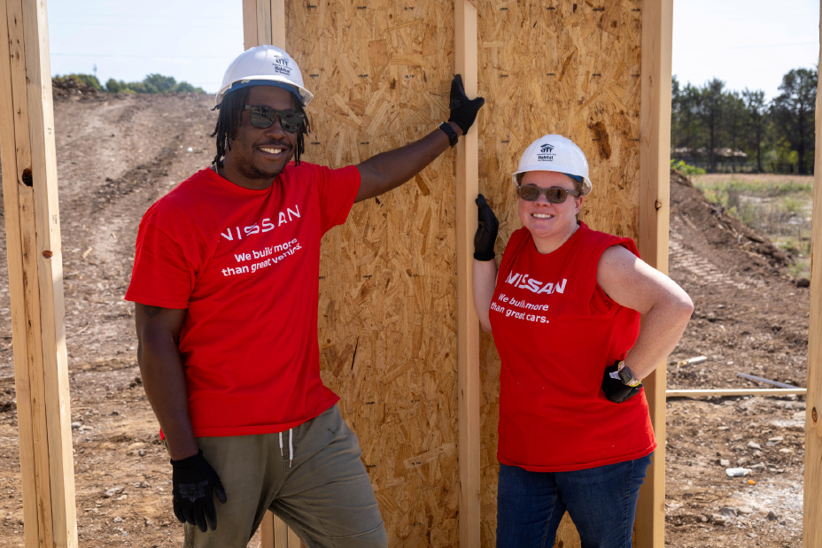 Two workers posing near a house frame outdoors.