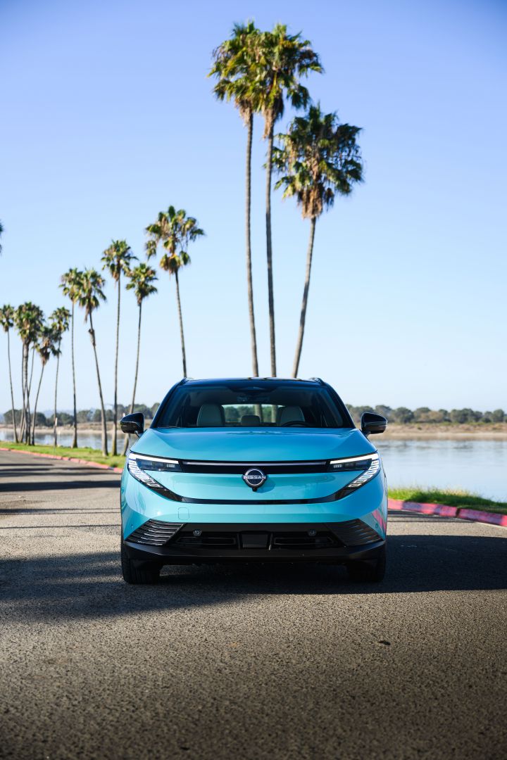 Front view of the 2026 Nissan LEAF parked on asphalt Infront of water and palm trees.