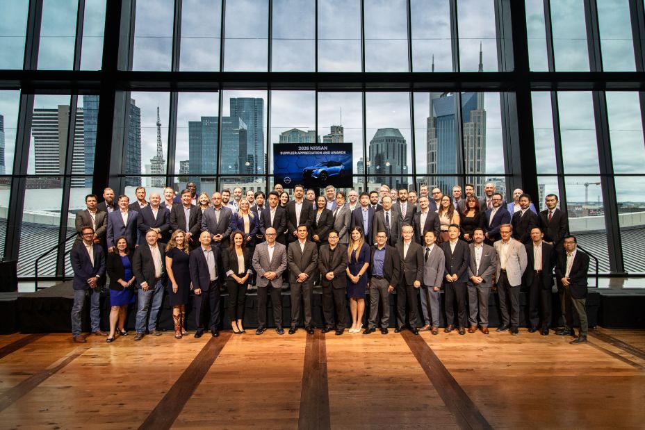 A group of people in business wear stand in front of a large window for a picture.