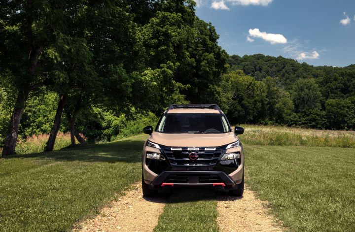 Front view of a 2025 Nissan Rogue rock creek parked on a dirt road in a field lined with pastures and trees around.