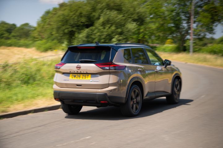 Nissan X‑Trail driving along a country road, shown from the rear, with a forest in the background.