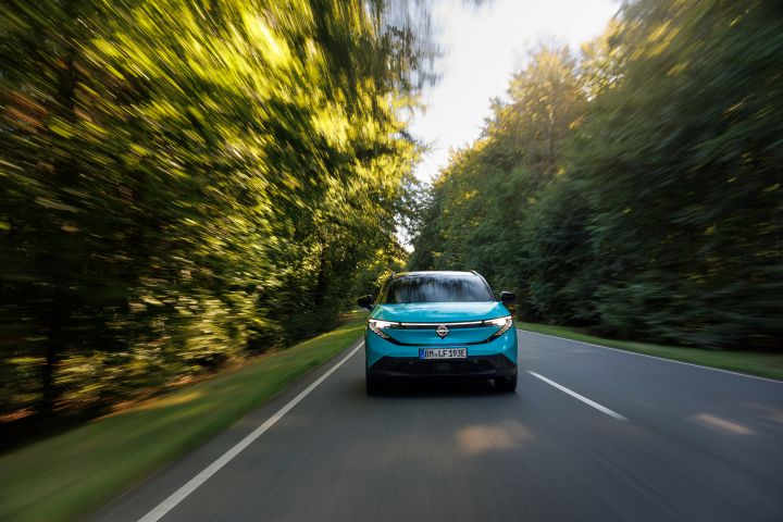 Ein türkiser Nissan LEAF fährt frontal auf den Betrachter zu, die Bäume neben der Straße sind durch die Geschwindigkeit unscharf
