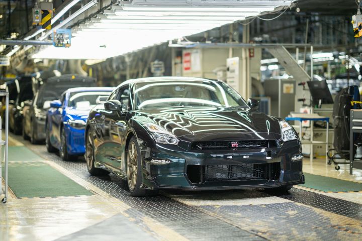 日産自動車 栃木工場の製造ラインにて、ミッドナイトパープルのR35 GT-Rが組立工程の途中で中央に配置されている。周囲には各種機械設備や作業台が並び、明るい照明の下で自動車製造が進行している様子。