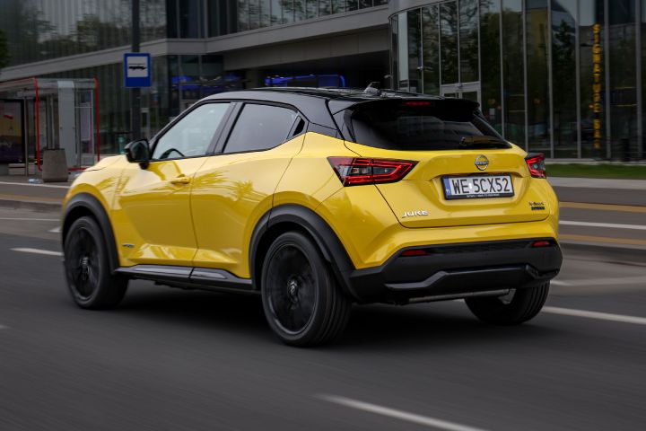 Jadący żółty Nissan Juke (widok z boku) z budynkiem w tle