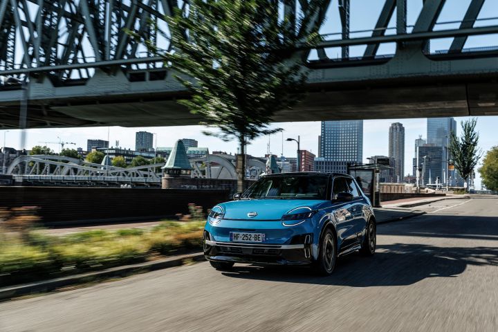 Dynamische 3/4 Frontansicht eines blauen Nissan Micra, der unter einer Bahnbrücke über eine Straße in Rotterdam fährt