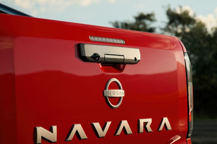 Close-up of the tailgate on a 2026 Nissan Navara ST‑X in Outback Red, showing the handle assembly, high-mounted lamp, Nissan badge, and large NAVARA lettering.