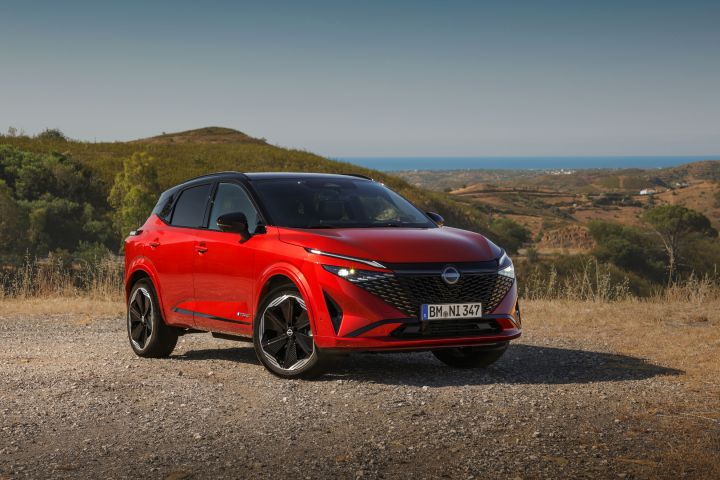 Nieuwe Nissan Qashqai in de kleur Fuji Sunset Red, schuin van voren gezien, geparkeerd op een heuvel