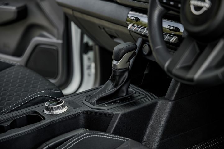 2026 Nissan Navara SL dual cab ute finished in Alpine White with a close interior view of the centre console, gear selector, rotary controller and nearby dashboard controls.