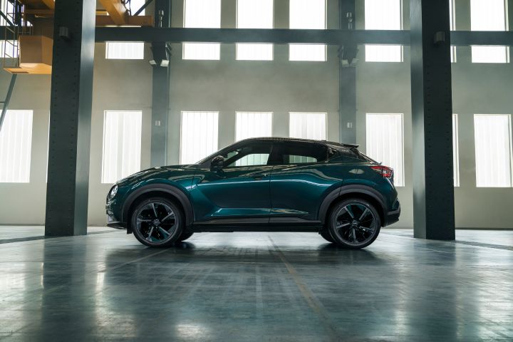 Side profile view of the Nissan JUKE Pulse parked indoors, highlighting its compact crossover silhouette, dark alloy wheels, and sculpted body lines.