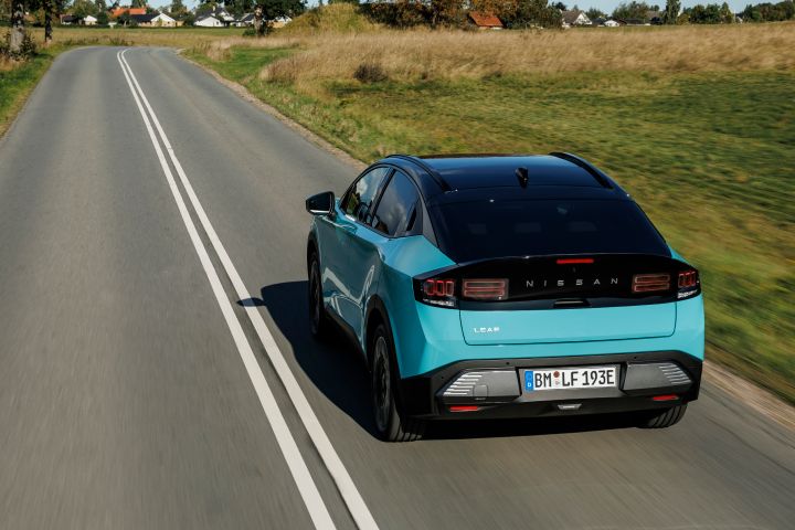 Blick von hinten aus erhöhter Position auf einen türkisen Nissan LEAF mit schwarz abgesetztem Dach und Rückfenster, das Auto fährt über eine dänische Landstraße