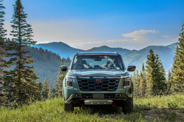 Front view of a 2025 Nissan Armada parked on lush grass overlooking pine tree scattered mountains.