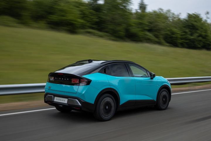 Vue arrière dynamique 3/4 d'une Nissan LEAF roulant sur une route devant une glissière de sécurité et un fond vert