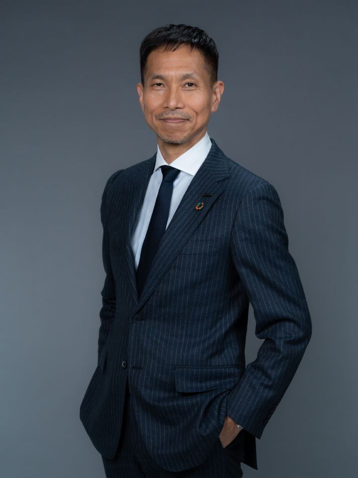 Portrait of Toru Ihara (suit, tie, NISSAN corporate pin and SDGs badge) (hands in suit pockets)