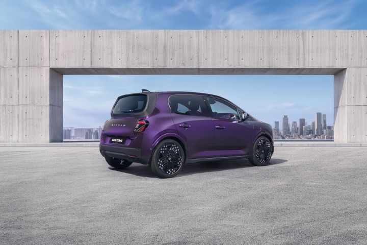 Tre fjärdedels baksida av en lila Nissan PIXO elektrisk stadsbil parkerad under en modern betongkonstruktion, med en stadssilhuett i bakgrunden.