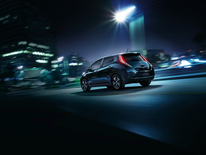 A steal navy Nissan LEAF driving in a city at night.