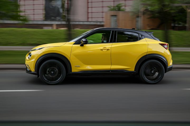 Jadący żółty Nissan Juke (widok z boku) z budynkiem w tle