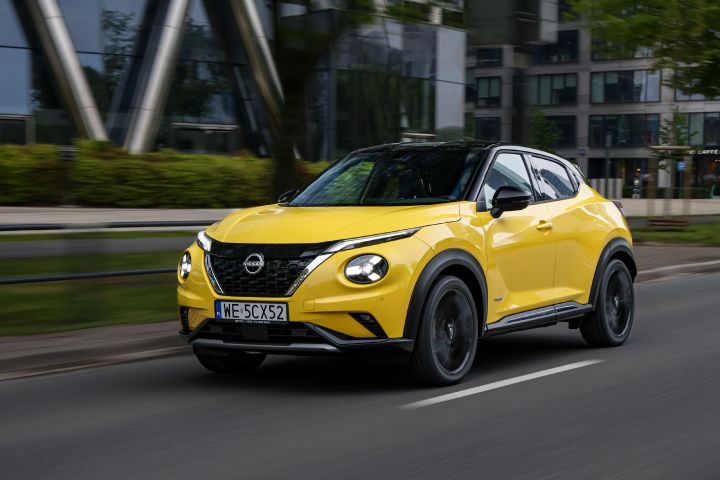 Jadący żółty Nissan Juke (widok z półprofilu) z budynkami w tle