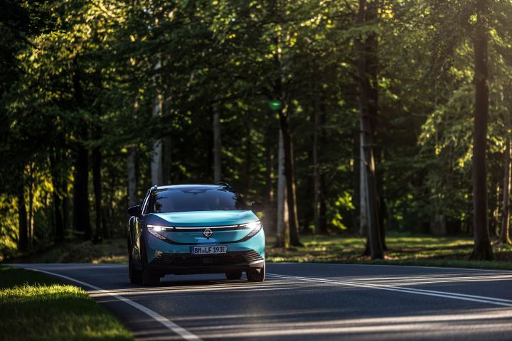 Ein türkiser Nissan LEAF fährt mit eingeschalteten Scheinwerfern aus einem dunklen Waldstück heraus