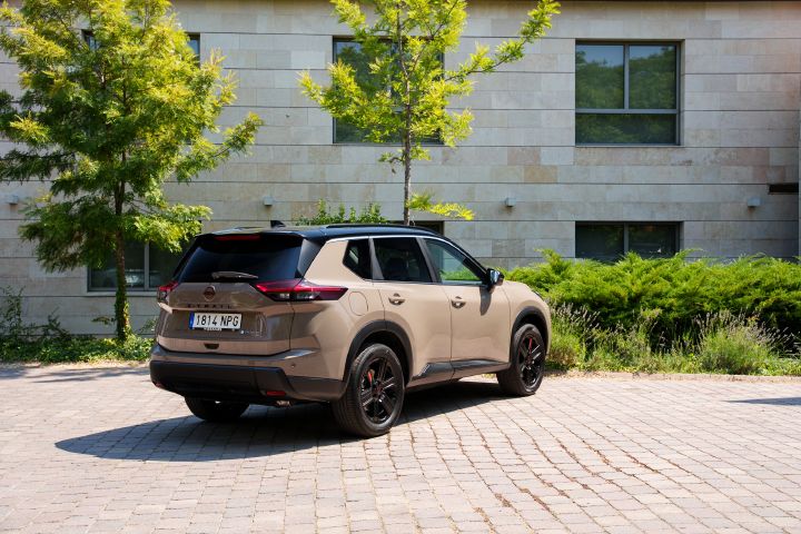 Dreiviertelansicht von hinten auf den Nissan X‑Trail. Im Hintergrund ein graues Gebäude
