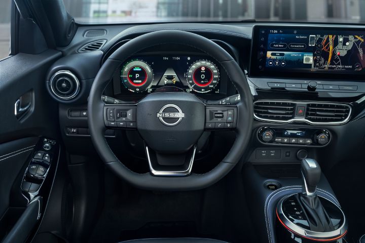 Driver’s view of the Nissan JUKE Pulse interior, featuring the steering wheel, digital instrument cluster, central touchscreen with navigation, and center console