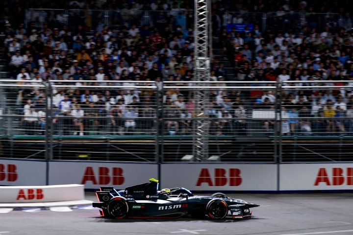 Seitenansicht von Oliver Rowland im Nissan e‑4ORCE 05 mit der Startnummer 1 auf der Rennstrecke während des Tokyo E-Prix, hinter ihm ist eine vollbesetzte Tribüne zu sehen.