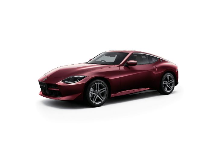 Burgundy Fairlady Z photographed in a light gray studio setting. The vehicle is shown from a front-left three-quarter angle, with the front end facing toward the left side of the image. The rich burgundy paint accentuates the coupe’s flowing body lines, while the sharp headlights and classic long-hood, short-deck proportions emphasize its sports car character. Silver alloy wheels complement the design, and the clean studio background highlights the vehicle’s distinctive styling and premium finish.