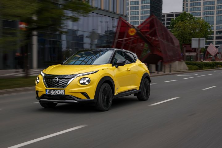 Jadący żółty Nissan Juke (widok z półprofilu) z budynkami w tle